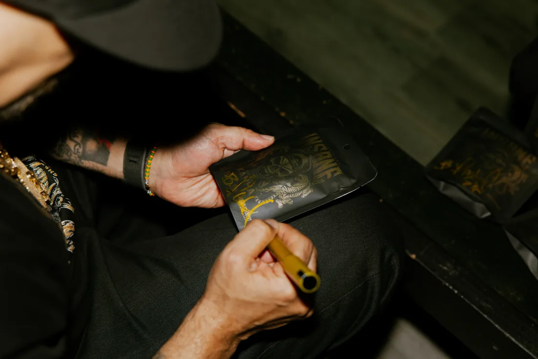 Signing an INSANE × KANHA pouch in gold marker